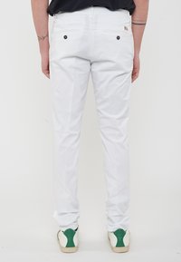 Pantaloni bianchi in cotone con una vestibilità dritta, dotati di due tasche posteriori con bottoni neri. Indossati con sneakers con dettagli verdi.