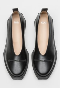 Scarpe in pelle nera con taglio basso, punta tonda e suola in gomma testurizzata. Presentano un branding discreto e una sottile fascia sulla parte superiore.