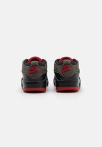 Zapatillas Nike Air que presentan una base de cuero negro, acentos grises, forro rojo y logo. El diseño incluye un cuello acolchado y suela de goma.