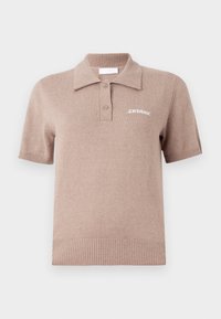 Kortermet beige polo-skjorte laget av mykt stoff. Har en ribbet krage, to knapper og en hvit brodert logo på brystet.