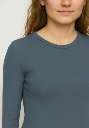 Langärmliges, geripptes Oberteil in gedämpftem Blau, mit rundem Ausschnitt und taillierter Passform. Weiches Material mit glatter Textur.