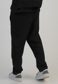 Mustad vabaaja püksid, millel on lõdva istuvus, küljetaskud ja elastsed varrukad, koos tekstuursete valgete tossudega hallide detailidega.