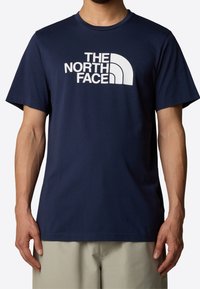 Navy blue cotton t-shirt featuring a white logo text and curved graphic. Short sleeves and round neckline with a smooth texture.