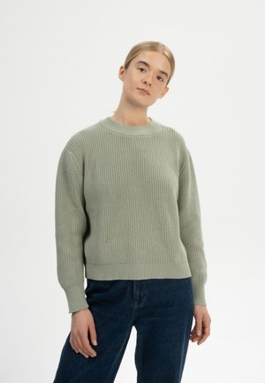 Helles grünes Strickpullover mit geripptem Muster, rundem Halsausschnitt und langen Ärmeln, kombiniert mit dunkelblauen Jeans.