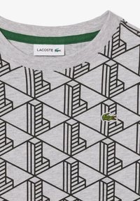 T-shirt grigio con motivo geometrico nero composto da forme sovrapposte. Accento verde all'interno del colletto e piccolo logo di coccodrillo verde.