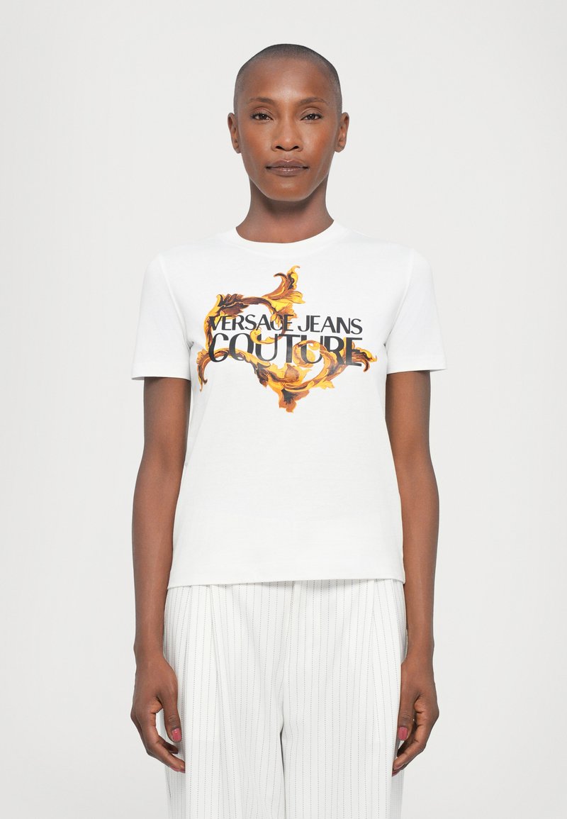 Balta kokvilnas t-kreklu ar krāsainu baroka stila drukājumu, kurā centrā ir izcēlts "VERSACE JEANS COUTURE" biezā melnā burtā.