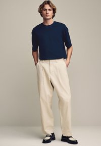 Camisa de manga corta azul marino combinada con pantalones de tela plisados en color crema y mocasines negros con un acento blanco. Tejido suave con un corte relajado.