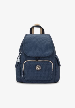 Námořnicky modrý batoh s chevronovým vzorem, přední kapsou na zip, bočními kapsami, béžovým a černým madlem na nošení a stříbrným přívěškem ve tvaru opice.