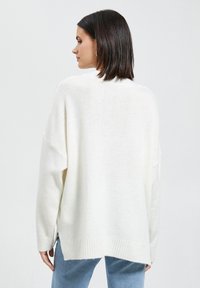 Biały oversize'owy sweter z teksturowanym splotem i ściągaczem na dole, z opadającymi ramionami i bocznymi rozcięciami dla swobody ruchu.