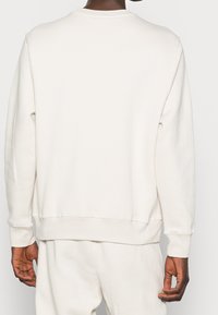Sudadera crema con cuello redondo, puños y dobladillo acanalados, fabricada en suave algodón y con detalles de costura mínimos; mostrada desde la parte posterior.
