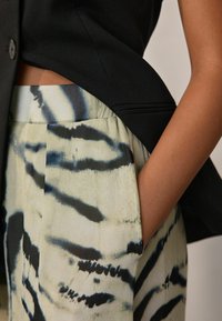 Blazer noir avec un revers incliné associé à un pantalon clair à motifs comportant des rayures noires sur un fond pâle. Poche latérale visible.