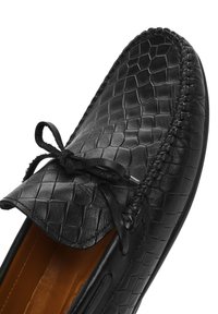 Schwarze Leder-Herren-Slipper mit reptilartiger Textur, dekorativer Schleife und gestepptem Rand. Das Innere verfügt über eine glatte braune Fütterung.