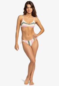 Set di bikini a righe con bralette triangolare e spalline regolabili, abbinato a un pantaloncino a vita bassa con lacci laterali. I colori includono rosa, verde e crema.