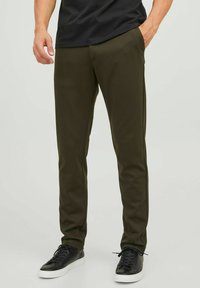 Pantalones verde oliva de corte ajustado, hechos de una tela suave. Cuentan con bolsillos laterales y se combinan con zapatillas negras sobre un fondo neutro.