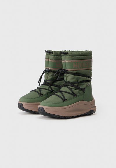 Par de botas de invierno aisladas en verde con cordones negros, suelas gruesas marrones y la marca "MOON BOOT" en el borde superior de cada bota.