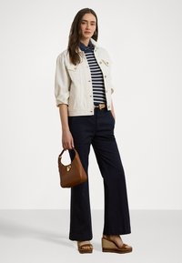 Biely denim kabát cez námornícky pruhované tričko, skombinovaný s tmavými rozšírenými nohavicami a hnedými sandálmi na klíne. Hnedá kabelka so zlatým hardvérom.