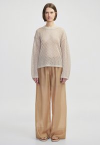 Maglione aperto beige chiaro con maniche ampie, abbinato a pantaloni beige larghi. Design semplice, texture morbida e vestibilità rilassata.