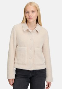 Lichtbeige cropped jack van textuurstof. Voorzien van een kraag, knoopsluitingen en twee voorkruimels. Eenvoudig ontwerp.