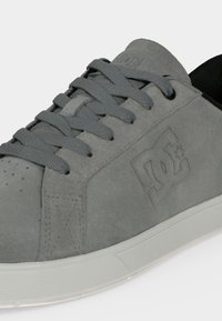 Γκρι sneaker από σουέτ με χονδρά κορδόνια, λευκή σόλα και ανάγλυφο λογότυπο DC στην πλευρά και στη γλώσσα, σε απλό λευκό φόντο.