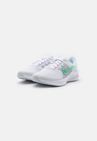 Scarpe sportive bianche con tomaia in mesh, dettagli viola e logo Nike verde. Presentano una suola ammortizzata e una presa testurizzata sulla suola esterna.