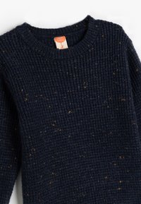 Sweter dzianinowy w ciemnym granacie z teksturowanym, ryżowym wzorem i brązowymi plamkami. Posiada okrągły dekolt oraz metkę z instrukcją pielęgnacji z tyłu.