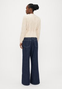 Μπεζ ριμπ πλεκτό πουλόβερ με εφαρμοστή μέση και φαρδιά μανίκια, συνδυασμένο με σκούρο μπλε τζιν παντελόνι φαρδιάς γραμμής με πίσω τσέπες και αντίθετες ραφές.