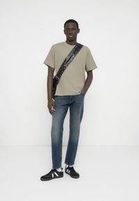 Καφέ ριπ κοντομάνικο πουκάμισο, τζιν παντελόνι και μαύρα αθλητικά παπούτσια με λευκές λεπτομέρειες. Το μοντέλο φορεί μαύρη τσάντα χιαστί με τρουκς.