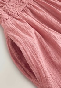 Rosa Leinenstoff mit strukturierter Oberfläche, ausgestattet mit gerafften Details an der Taille und weichen, fließenden Falten.