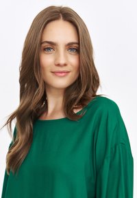 Zielona, luźna bluzka wykonana z miękkiego materiału, z okrągłym dekoltem i długimi rękawami, charakteryzująca się gładką fakturą i minimalistycznym wzornictwem.