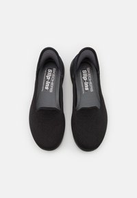 Musta liukuvat kengät, joissa on teksturoitu päällinen, joustavat sivupaneelit ja pehmustettu sisäpohja, sisältä löytyy logo "Skechers Slip-Ins".