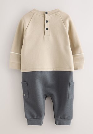 Beżowa bluzka z długim rękawem z ciemnymi guzikami; szare spodnie z bocznymi kieszeniami; miękki bawełniany materiał; kontrastowe przeszycia. Odpowiednie na codzienne noszenie.