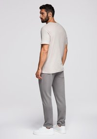 Lichtgrijs t-shirt met korte mouwen, gecombineerd met bijpassende grijze joggingbroek. Model draagt witte sneakers en staat met de rug naar de kijker. Gladde stoftextuur.