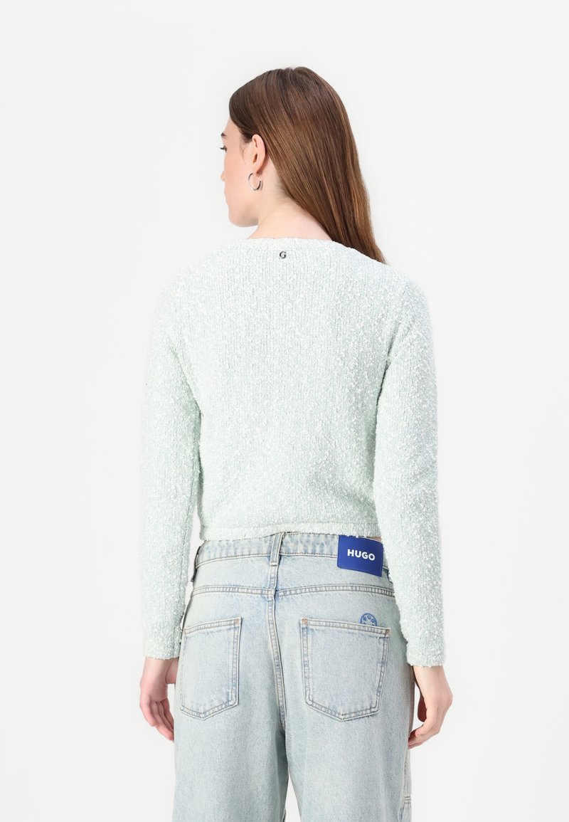 Helles, grünes, strukturiertes Sweatshirt mit langen Ärmeln, Rundhalsausschnitt und einem kleinen Logodetail auf der Rückseite, kombiniert mit hochgeschnittenen, hellblauen Jeans.