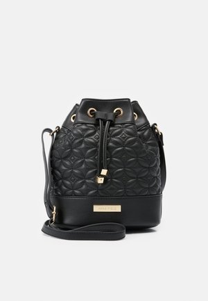Sac seau en cuir matelassé noir avec œillets dorés, fermeture à cordon, bandoulière réglable et plaque nominative « Anna Field » en bas à l'avant.