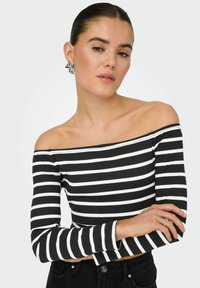 Sort og hvid stribet off-the-shoulder top med lange ærmer, ribbet tekstur, parret med sorte højtaljede bukser og en dekorativ ørering.