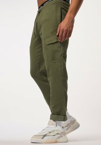 Olijfgroene cargobroek met zijzakken, een verstelbare taille met trekkoord, taps toelopende pasvorm en opgerolde enkels, gecombineerd met witte en beige sneakers.