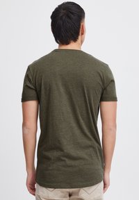 T-shirt à manches courtes vert olive avec col rond, fabriqué en tissu doux. Présente un ourlet légèrement courbé et des manches retroussées.