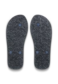 Sorte flip-flopsål med tekstureret geometrisk mønster og tre blå cirkulære stikpropper på hver sål, vist fra bunden.