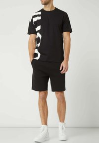 T-shirt noire avec un grand motif blanc, associée à un short noir et des baskets montantes blanches. Design simple, coupe confortable et style décontracté.