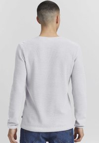 Langärmliger weißer strukturierter Pullover mit Rundhalsausschnitt, ausgestattet mit einem gerippten Design und taillierten Bündchen. Getragen mit blauen Jeans.