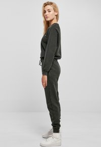 Mørk grå joggedress med lange ermer og elastisk liv, med snor. Kombinert med hvite høye sneakers. Glatt tekstur.