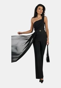 Jumpsuit nero a spalla unica con pannello in satin fluido, vita sfiancata con dettagli in metallo dorato e design a gamba larga sartoriale.