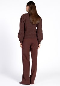 Bruine fluffy trui met pofmouwen, gecombineerd met hoog-uitgesneden donkerbruine broek. Glad materiaal en een relaxte pasvorm.