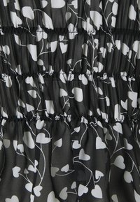 Tissu noir avec motif de cœurs blancs et de vignes ; présente une texture froncée et des coutures élastiquées pour un effet ajusté. Matière douce et légère.