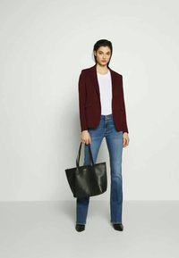 Blazer burdeos sobre una camiseta blanca, combinado con unos jeans acampanados azules. Sosteniendo un bolso de mano de cuero negro. Diseño elegante y minimalista.