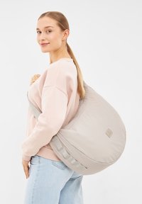 Borsa a spalla in nylon grigio chiaro con una texture liscia e forma arrotondata, dotata di una larga tracolla e un discreto dettaglio del logo. Indossata sulla spalla.