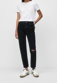 Černé džíny s uvolněným střihem, s roztrženými koleny, spárované s jednoduchým bílým tričkem a bílými teniskami se šedými a černými akcenty.