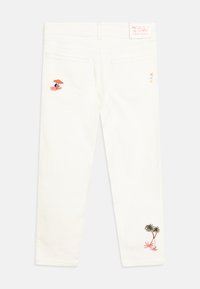 Jeans in denim bianco con disegni ricamati: una scena di spiaggia con un ombrellone sulla tasca sinistra e palme sulla tasca destra.