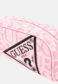 Rosa tekstureret rektangulær penalhus med mønster af hvid og lys rosa GUESS-logo, der har en sort trekantet logoapplikation. Med lynlåslukning.