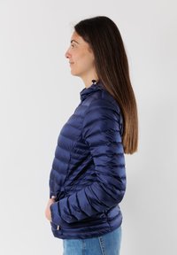 Giacca a vento blu navy imbottita con cuciture orizzontali, colletto alto e tasche con zip. Materiale leggero con una superficie liscia e lucida.